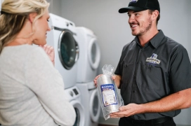 Commercial dryer vent cleaner showing business owner new dryer vent hose while standing in front of stacked dryers.