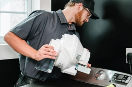 Male Dryer Vent Wizard professional installs a new booster fan behind residential dryer.