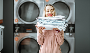 Young woman enjoying clean ironed clothes in the self serviced laundry with dryer machines on the background